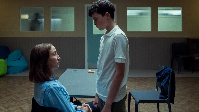 A boy stands over a woman in a chair.