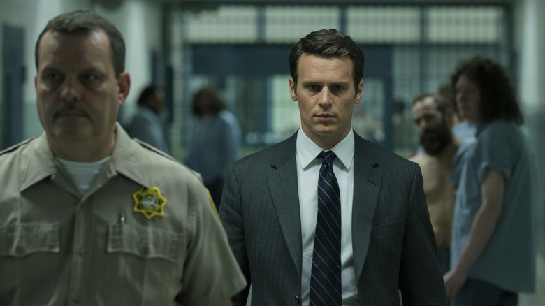 A detective walks down the hall of a prison escorted by a guard