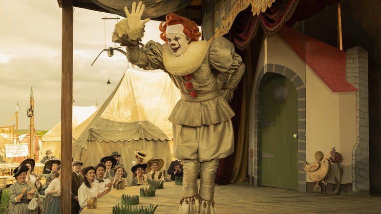 Pennywise the clown waving to a crowd during a flashback in Welcome to Derry