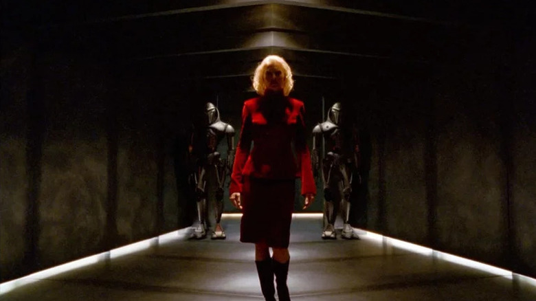 Number Six (Tricia Helfer) walks down a darkened hallway flanked by Cylons in Battlestar Galactica (2003)