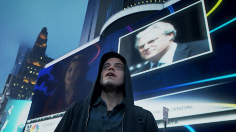 Elliot Anderson (Rami Malek) stands in front of a large video screen in Mr. Robot