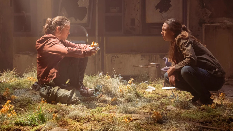 A seated Ellie (Bella Ramsey) speaks to a crouched Tess (Anna Torv) in The Last of Us