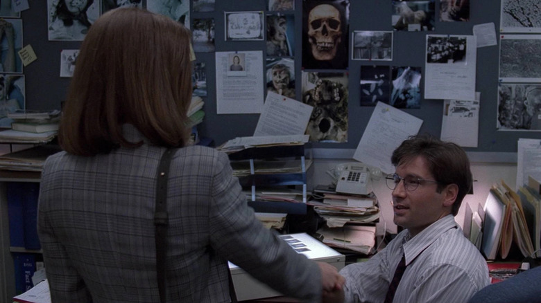Dana Scully (Gillian Anderson) shakes hands with Fox Mulder (David Duchovny) in his office in The X-Files