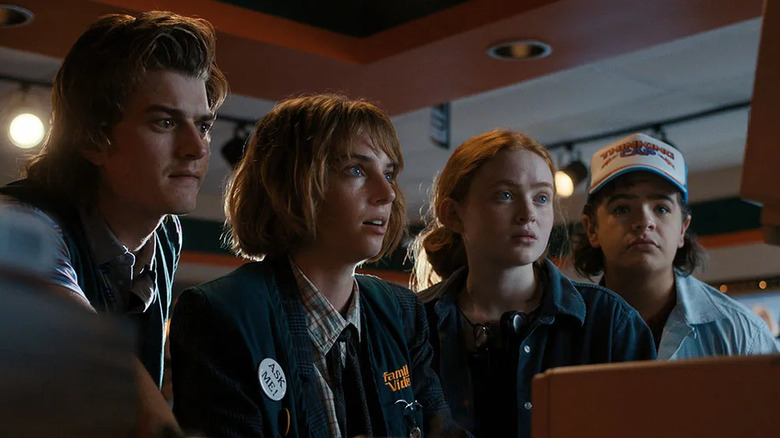 Joe Keery as Steve, Maya Hawke as Robin, Sadie Sink as Max, and Gaten Matarazzo as Dustin looking at a computer in Stranger Things