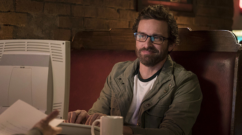 Chuck Shurley (Rob Benedict) smiles while typing on a computer in Supernatural