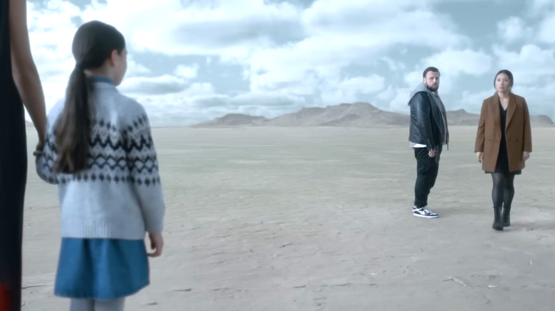 A little girl greets a man and a woman in the desert.