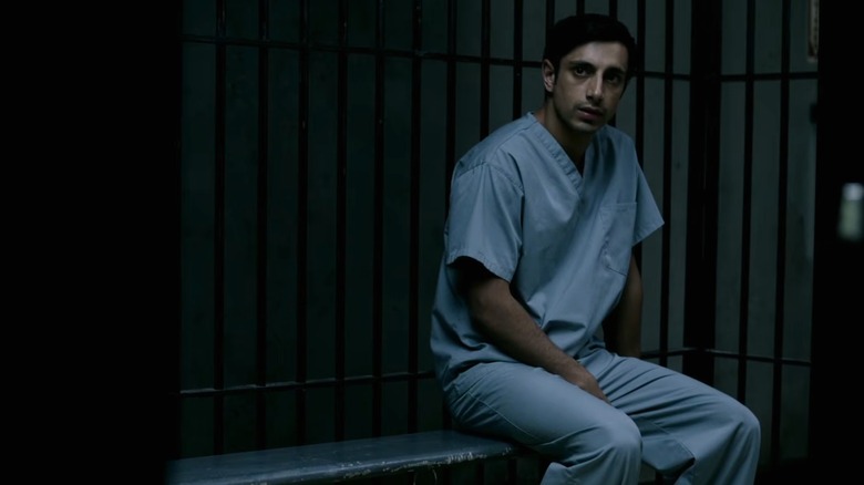 Naz in blue prison uniform sitting in cell