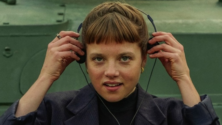 Kleo Straub putting on headphones with a smirk in Kleo