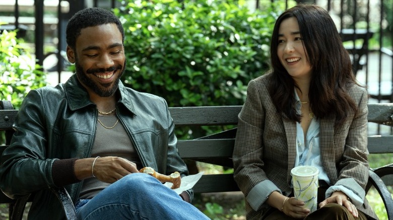 John and Jane Smith smiling while sitting on a park bench in Mr. & Mrs. Smith