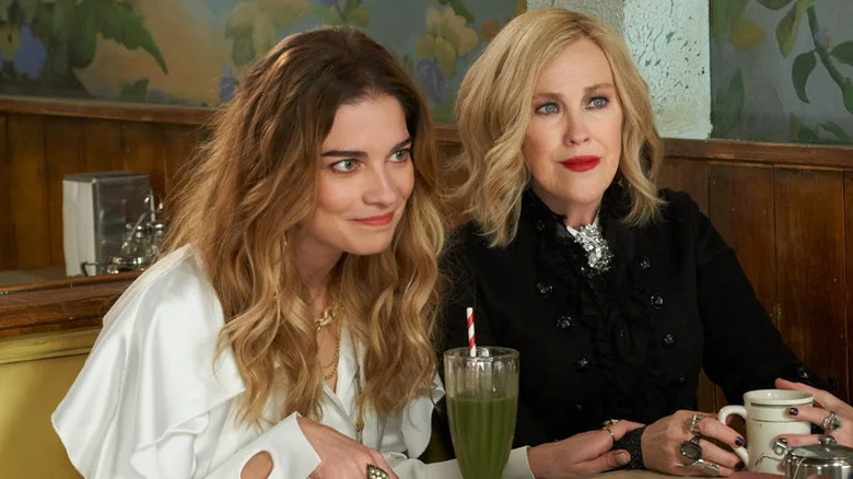 Alexis Rose (Annie Murphy) and Moira Rose (Catherine O'Hara) sit listening attentively in a booth in Schitt's Creek