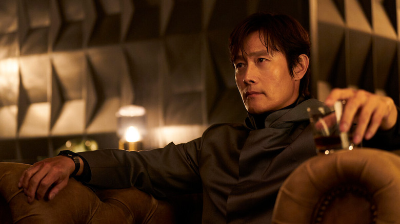 Lee Byung-hun as the Front Man, sitting in a chair with a drink in Squid Game.