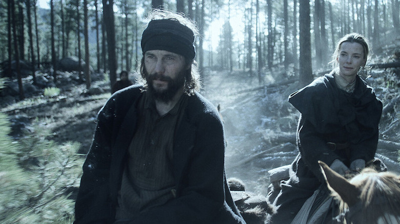 A weary Isaac Reed (Taylor Kitsch) and Sara Rowell (Betty Gilpin) ride on horseback through a forest in American Primeval