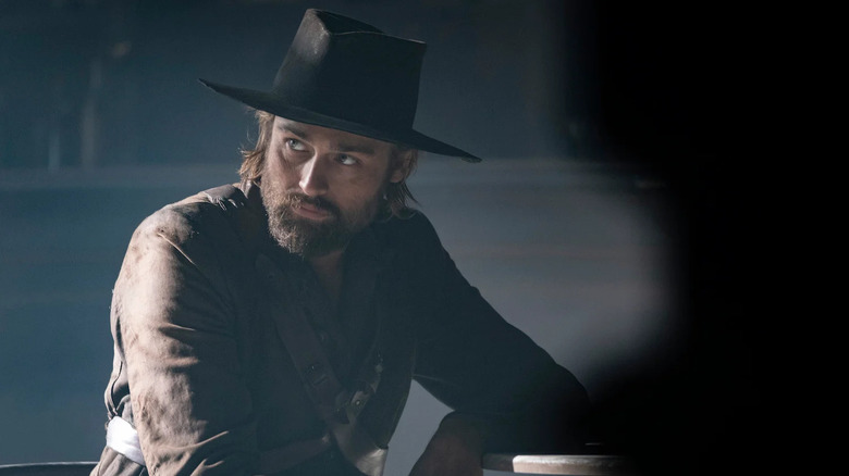 Red Bill (Douglas Booth) sits in a dimly lit room in That Dirty Black Bag