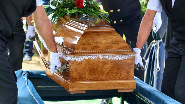Wooden coffin being lowered by people with white gloves