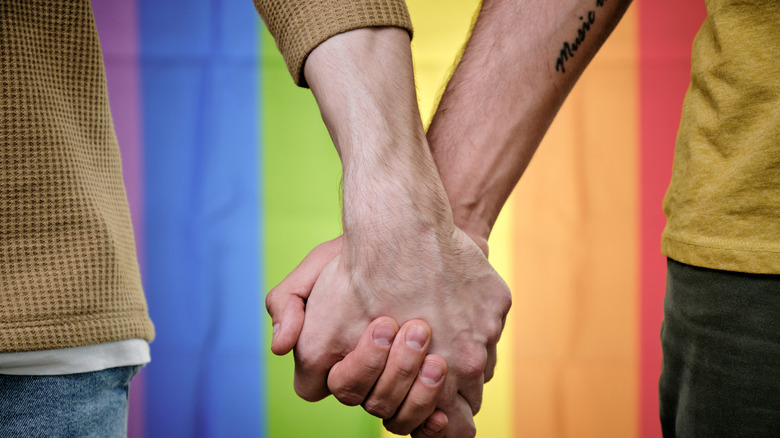 Close-up of two men holding hands in front of rainbow flag