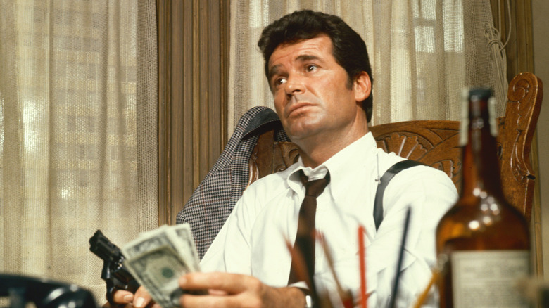 James Garner as Jim Rockford sitting at his desk holding money and a gun, with a bottle of liquor in the foreground