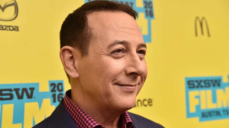 Paul Reubens standing against yellow background and smiling