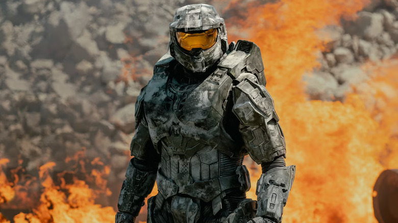 Pablo Schreiber as Master Chief in his iconic armor standing in front of a fire in Halo
