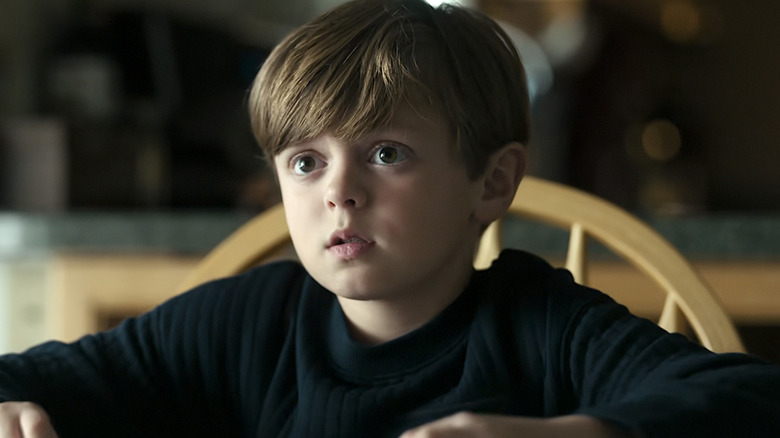 The Son wearing a black shirt sitting in a wood chair in The Night Agent