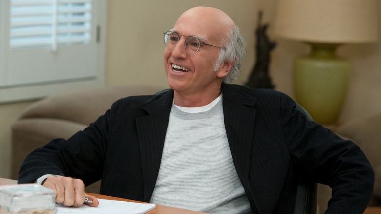 Larry David sorrindo em sua mesa conversando com Jerry Seinfeld em Curb Your Enthusiasm