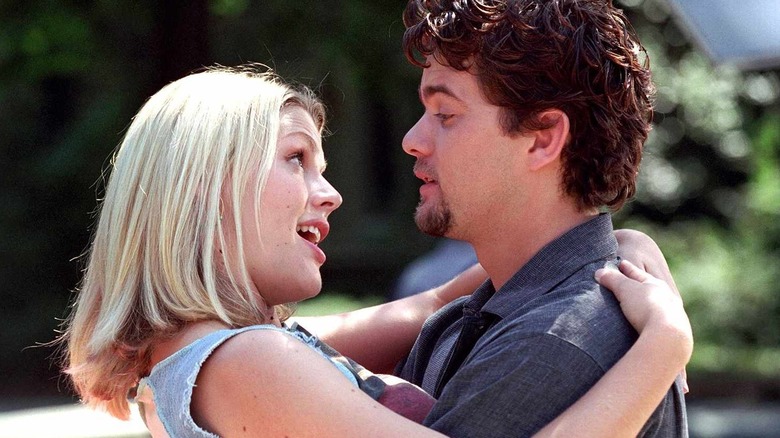 Audrey (Busy Phillips) e Pacey (Joshua Jackson) se abraçam e se olham nos olhos em Dawson Creek com árvores ao fundo
