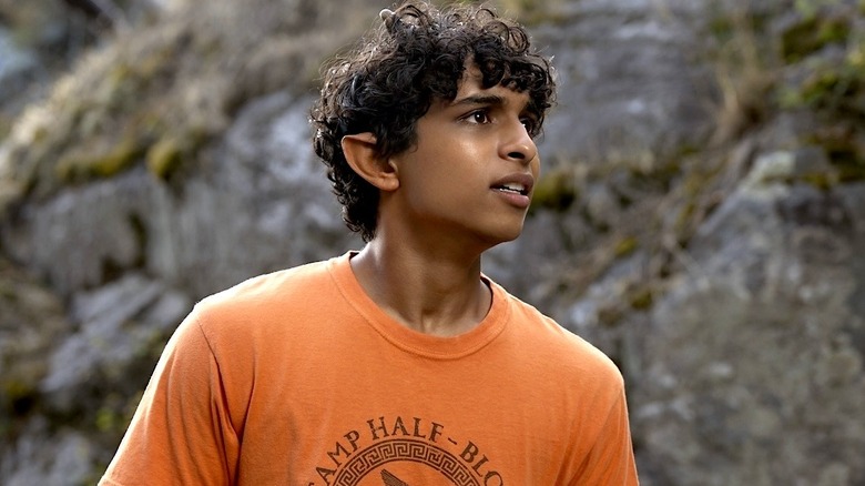 Grover wearing an orange Camp Half-Blood t-shirt looking to the side