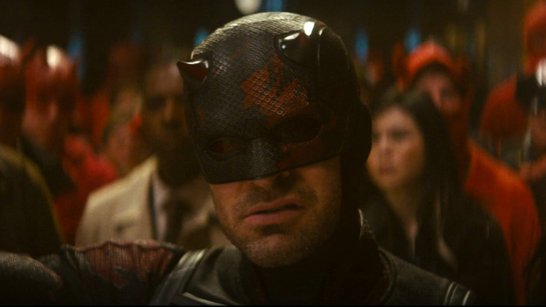 Charlie Cox as Daredevil in the black costume, with scratches revealing the red underneath.