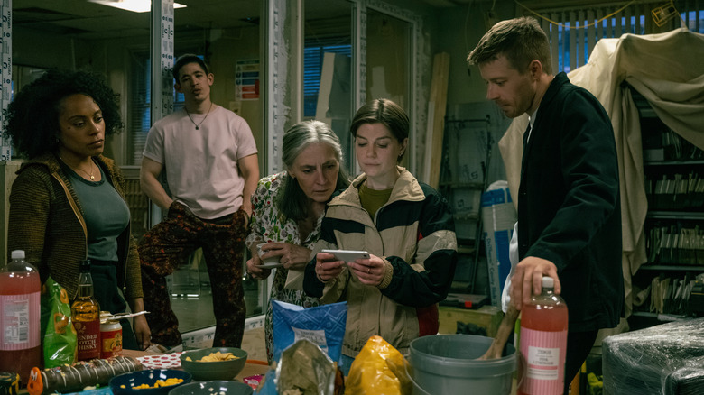 Lou (Rosalind Eleazar), Roddy Ho (Christopher Chung), Standish (Saskia Reeves), Shirley Dander (Aimee Ffion-Edwards), River (Jack Lowden) looking at a phone in the Slough House office in Slow Horses