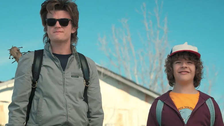 Steve Harrington dons sunglasses with a backpack and a bat, standing next to Dustin Henderson in "Stranger Things 2" (2017)