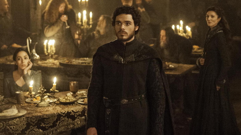 Oona Chaplin as Talisa, Richard Madden as Robb, and Michelle Fairley as Catelyn staring up in a dining hall in Game of Thrones