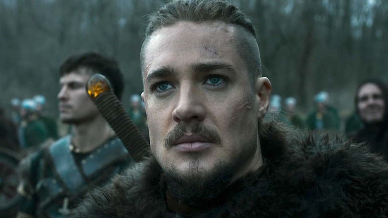 Closeup of Uhtred in a fur coat with his allies in the background in The Last Kingdom