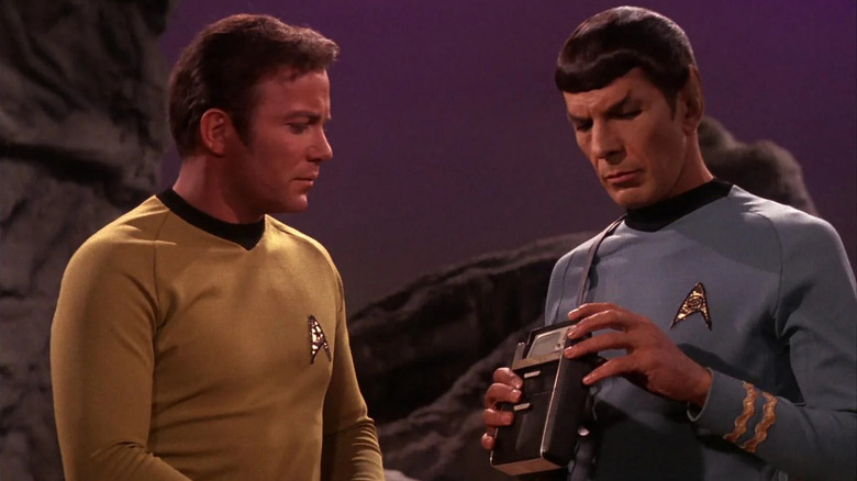 Captain James T. Kirk (William Shatner) stands next to Mr. Spock (Leonard Nimoy), who is holding a Tricorder in "Star Trek: The Original Series"