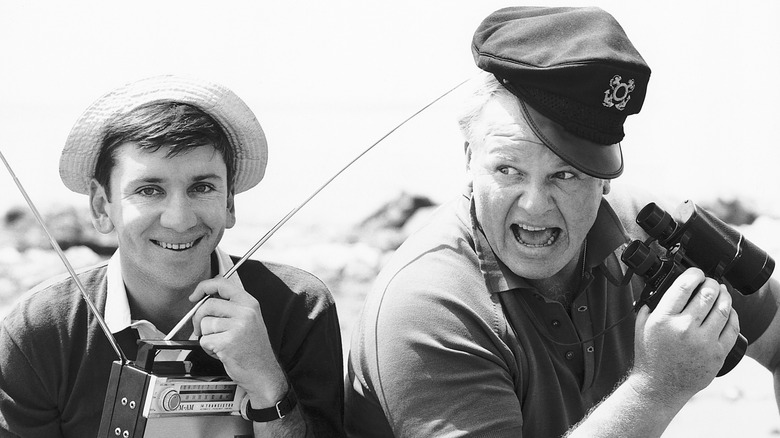 Bob Denver as Gilligan holding a radio and smiling, and Alan Hale Jr. as Skipper holding binoculars and shouting