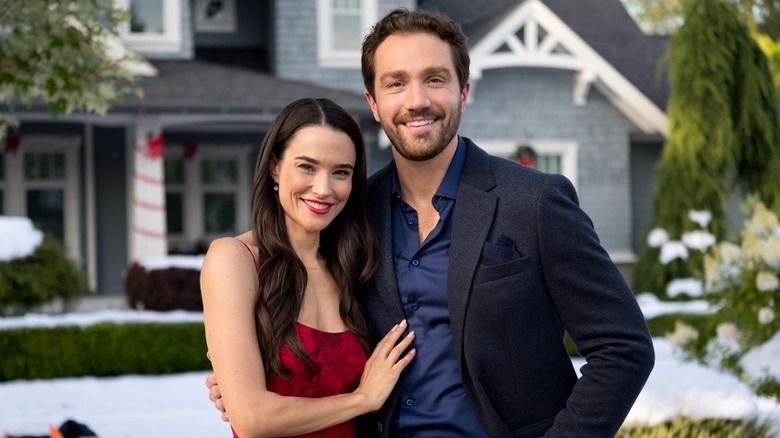 Julie posing next to Mark in front of a grey house with Christmas decorations