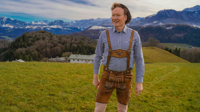Conan O'Brien stands in a field dressed in lederhosen