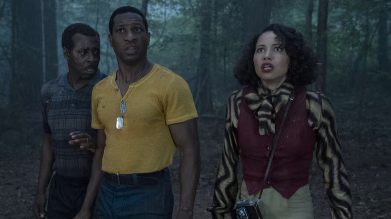 Three people stand looking terrified in the woods