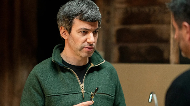 Nathan Fielder speaks with a man while holding a pen.