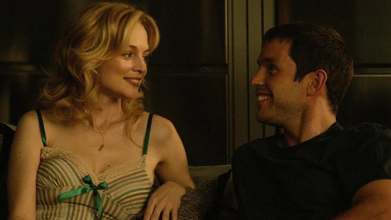Emily, wearing a frilly tank top, smiles at her boyfriend in a dark, paneled room