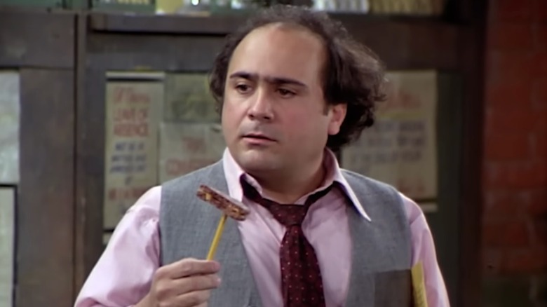 Louise De Palma in "Taxi," wearing a shirt, with a loose tie and vest and holding up a biscuit with a pencil.