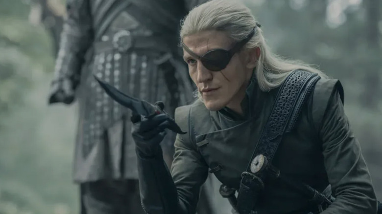 Ewan Mitchell as Aemond Targaryen holding a knife and wearing an eyepatch while crouching in House of the Dragon