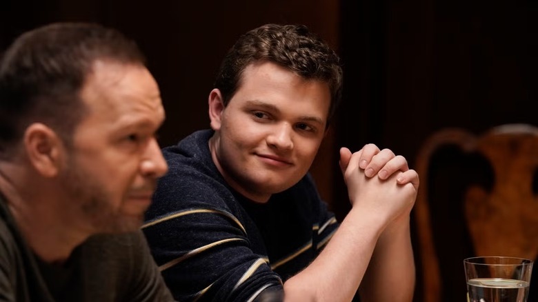 Andrew Terraciano, Sean Reagan rolünde, lacivert beyaz çizgili bir kazak giyiyor, babasına sevgiyle bakıyor ve yanında oturuyor; Donnie Wahlberg, Danny Reagan rolünde, kahverengi bir kazak giyiyor, odak dışı, Blue Bloods'da ön planda.