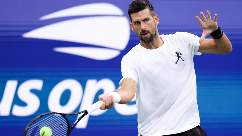 Novak Djokovic hitting a tennis ball in front of a U.S. Open sign