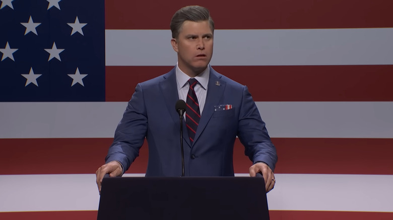 Colin Jost standing behind a podium on SNL