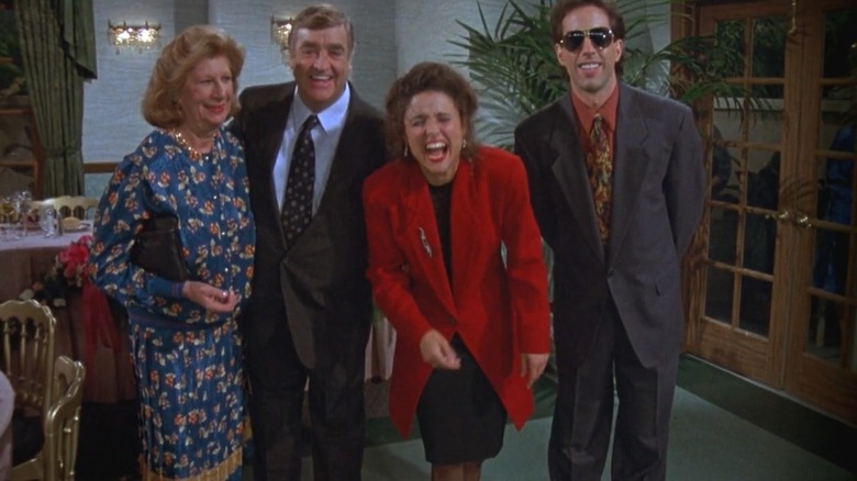 Elaine laughs while wearing a red jacket while Jerry stands beside her and his parents in "Seinfeld"