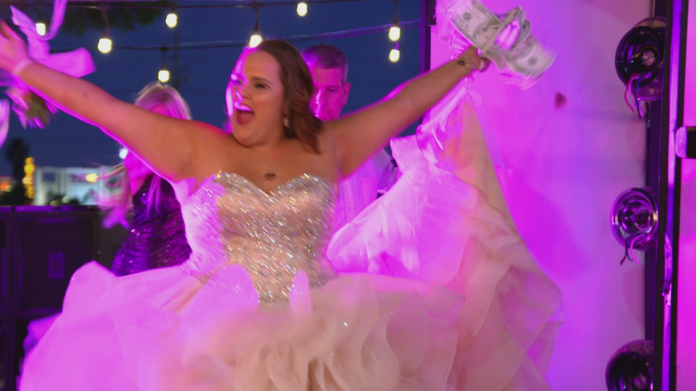 A young woman in a glittery ball gown throws her arms up with cash in hand in My Super Sweet Sixteen