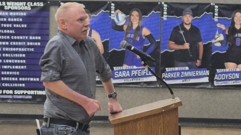 A recent photo of John Thompson speaking at a podium in a high school gym