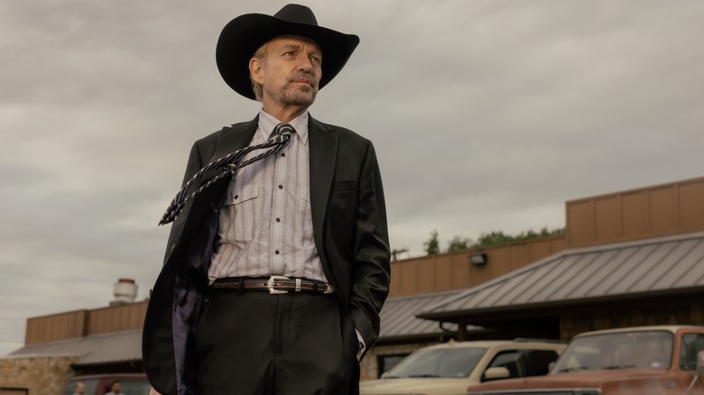 Billy Bob Thornton as Tommy in Landman stands outside a restaurant against a gray sky