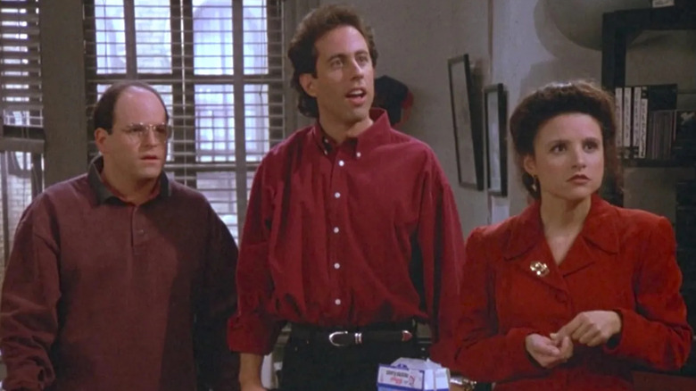 George (Jason Alexander), Jerry (Jerry Seinfeld), and Elaine (Julia Louis-Dreyfus) stand in Jerry's apartment, looking off to the right in shock in Seinfeld