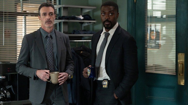 Reid Scott as Det. Riley and David Ajala as Det. Walker stand and hold mugs in Law and Order