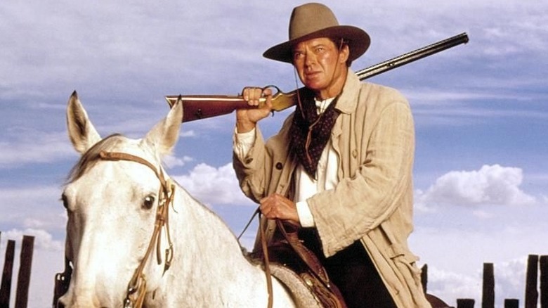The Lazarus Man riding a horse with a rifle resting on his shoulder